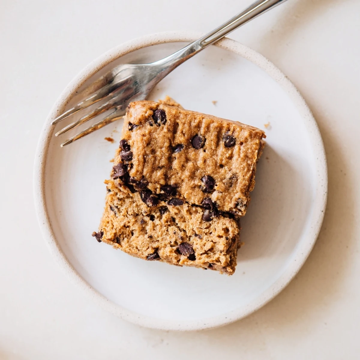 Golden flourless peanut butter banana bars studded with melted dark chocolate chips on a white plate