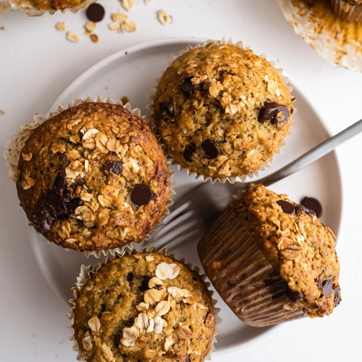 Warm homemade banana chocolate chip muffins with oats resting on a wooden cutting board, one sliced open to reveal the moist banana-filled interior and pockets of melted chocolate
