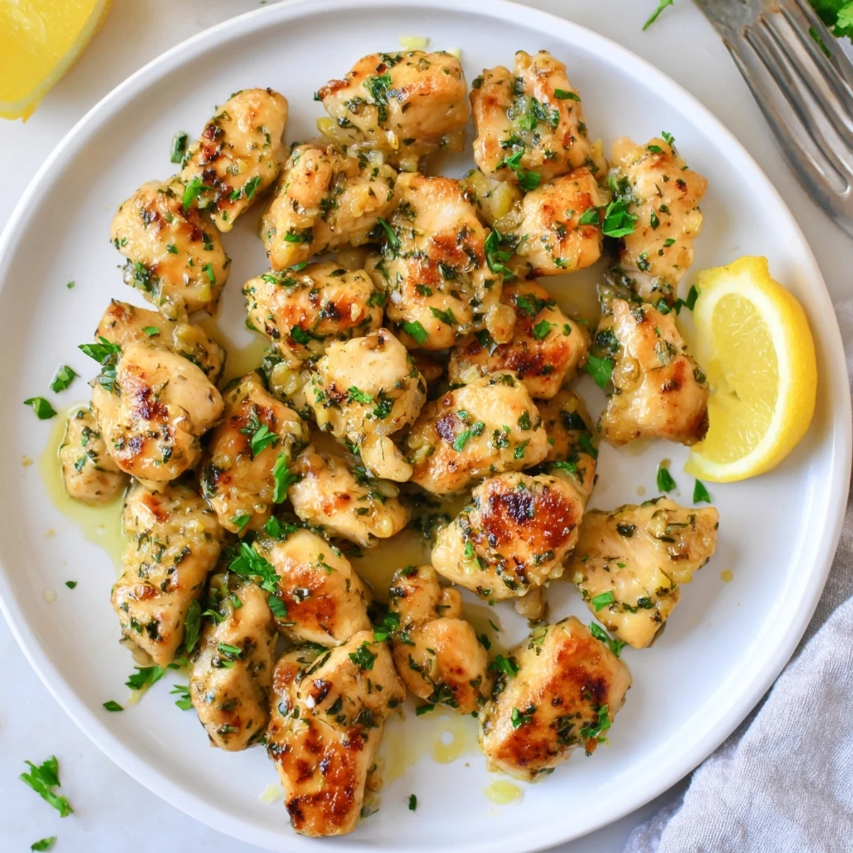 Golden pan-fried garlic butter chicken bites garnished with fresh parsley and lemon wedges