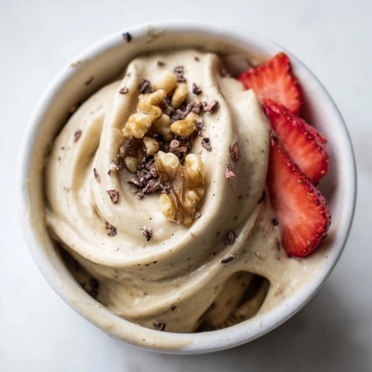 Creamy healthy nice cream recipe scooped into bowls topped with fresh fruit slices and chopped nuts