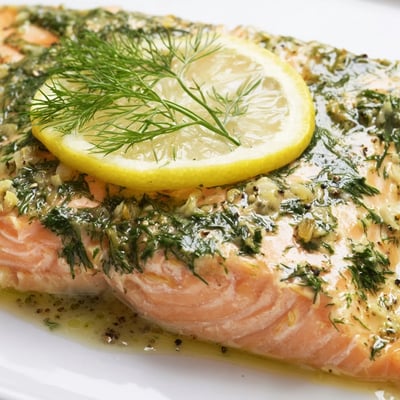 A close-up of tender baked salmon with lemon and dill weed, topped with fresh green herbs.