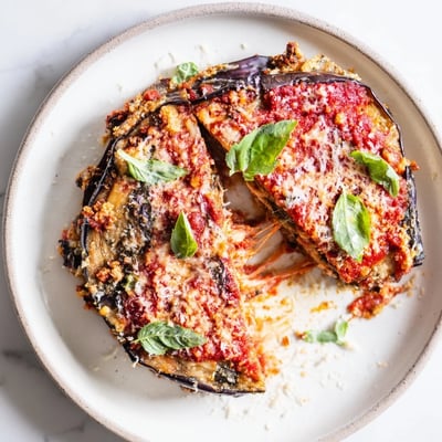 Slices of smoky charred aubergine layered with Parmesan and fresh basil on a marble countertop.  