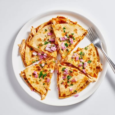 A close-up view shows the crispy tortilla wedges of Hot Honey BBQ Chicken Quesadillas served with a side of sour cream. 