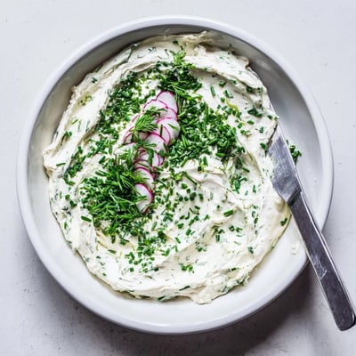 A close-up of Simple Easter Herb Cheese Dip beside crisp carrot sticks and crackers for dipping at a spring gathering.